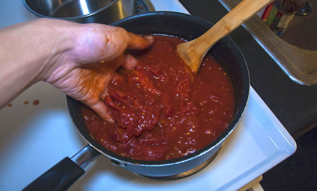 person with hand in marinara sauce